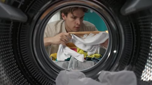 View From Inside the Washing Machine Young Man Takes Out the Dirty Colorful Clothes From the Drum