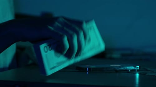 Close-up of a woman's hands stacking and arranging US dollar bills on a table under moody blue