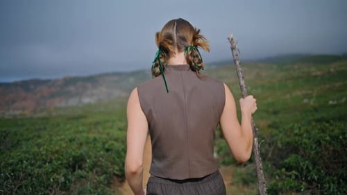 Woman Journeying Green Hill with Stick Alone Rear View Serene Girl Walking Path
