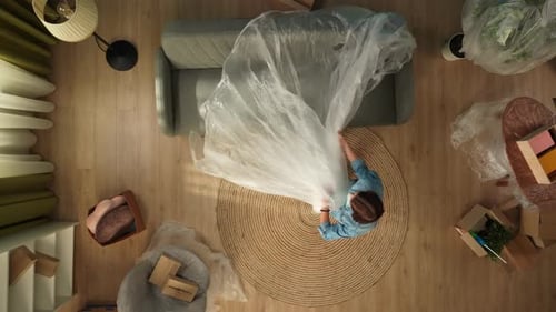 Top View of Apartment Living Room Woman Coming in Room Taking Off Film From Sofa and Cleaning It