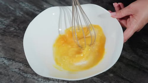 Primer plano del chef batiendo huevos en un tazón blanco para prepararlos para hornear