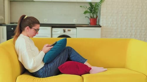 Woman Uses Phone Sitting on a Yellow Couch