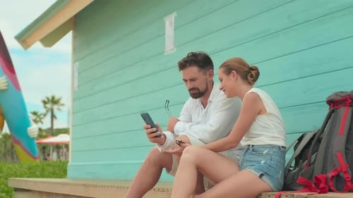 Young Couple Laughing while Looking Through Photos in Mobile Phone at Resort