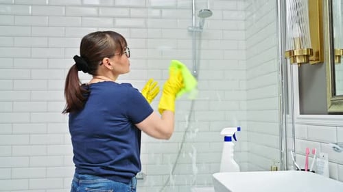 Woman Cleans Glass Shower Wall in Bright Bathroom