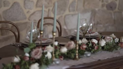 Rustikaler Hochzeitstisch für den Innenbereich mit floralem Tafelaufsatz und hohen Kerzen.