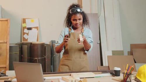 Woman Sands Wood at Workbench in Workshop