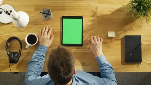 Top View of Young Creative Man Working on His Green Screen Tablet Computer Sitting at His Desk. He