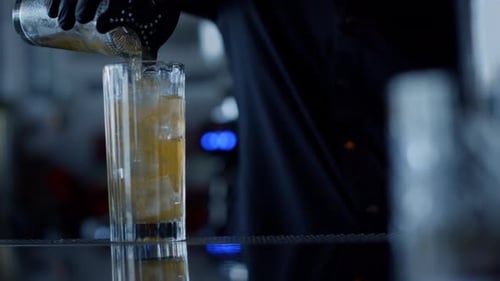 Bartender prepares cocktail with ice at dark bar