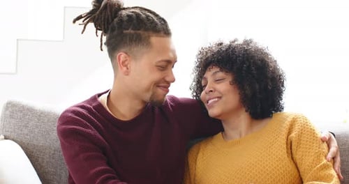 Después de cálidas miradas, pareja afroamericana se apoya en el sofá de la sala y sonríe a la cámara