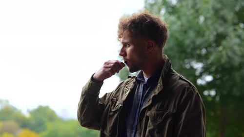 Vue latérale d'un jeune bel homme caucasien fume une vape à l'extérieur, un homme décontracté et attentionné fumant