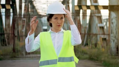 Confident Woman Engineer in Workwear and Hard Hat Standing Near Metal Bridge Construction and Put on