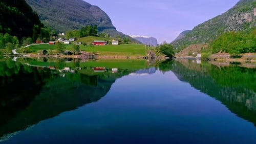 Aerial drone forward moving shot over lake with houses surrounded by mountain range on a sunny day.