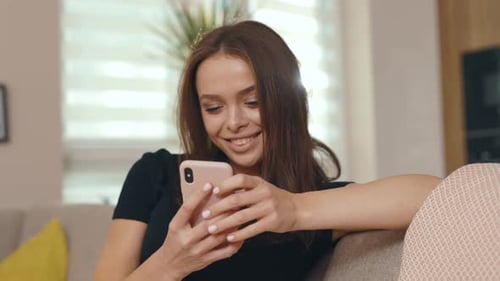 Smiling woman using phone on sofa at home