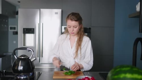 Caucasian Woman Making a Salad of Vegetables and Tasting a Meal on a Stove on Modern Kitchen Island