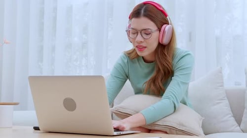 Young asian woman enjoy music while wearing headphones and working on laptop computer.