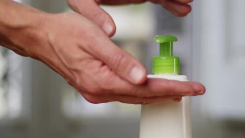 Young Man Squeezing a White Moisturizer From a Tube on His Hand Closeup Morning Routine Beauty and