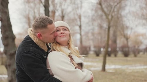 Glückliches verliebtes Paar, das zusammen im Freien in einem Winterpark spazieren geht. Der Ehemann umarmt sanft seine
Frau