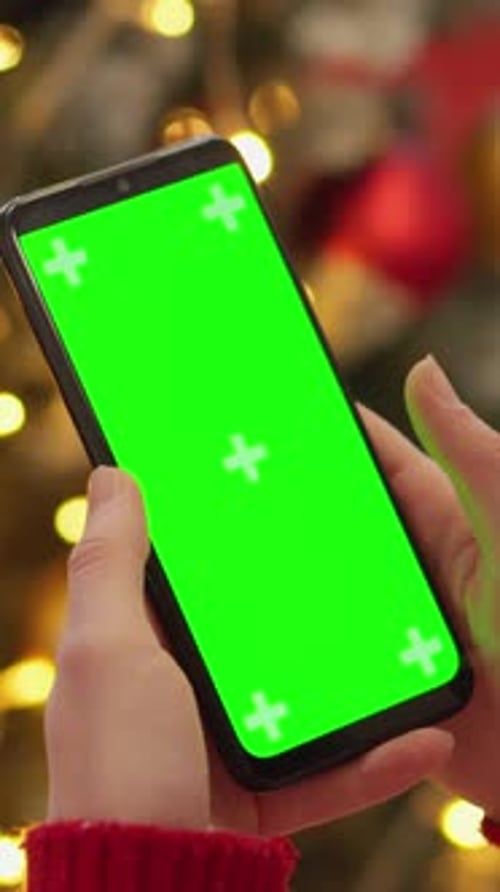 Hands Holding Phone with Green Screen by Christmas Tree