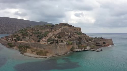 Fly along with the drone as it approaches the old forts on an island, with a view of the mountains i