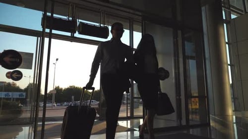 Businessman with His Female Colleague Walking Through Enter to Terminal and Roll Suitcase on Wheels