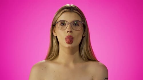 Joven caucásica descarada saca la lengua, fondo morado aislado