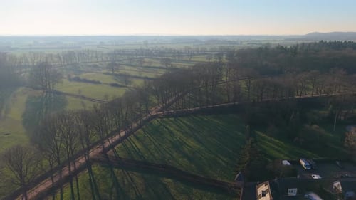 Aerial view of winter farmland with leafless trees, hedgerows, and winding road casting long shadows