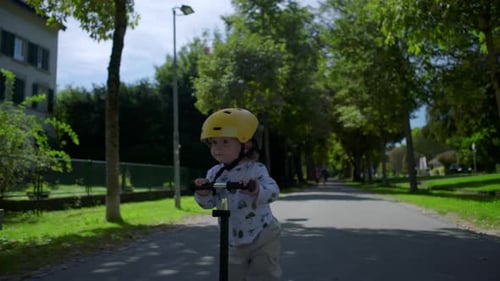 Toddler riding scooter with yellow helmet on park path, childhood play and adventure, outdoor
