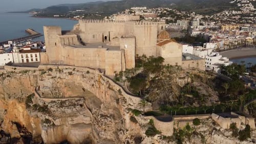 Peniscola castle along Spain's coastline overlooks the picturesque harbor - aerial reveal