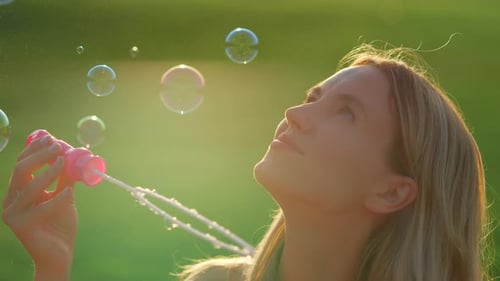 Portrait of Young Woman Blowing Soap Bubbles in City Park. Closeup Charming