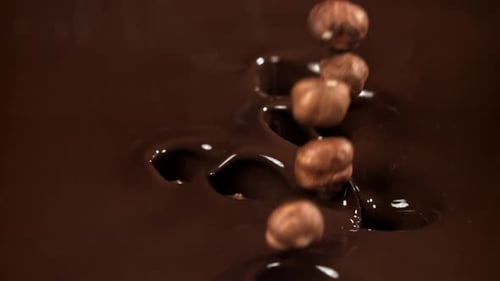 Hazelnuts Falling into Dark Chocolate in Slow Motion