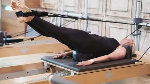 Effective Pilates Exercise in Gym Woman Lying on Inflatable Ball on Reformer Spreading Legs to Sides