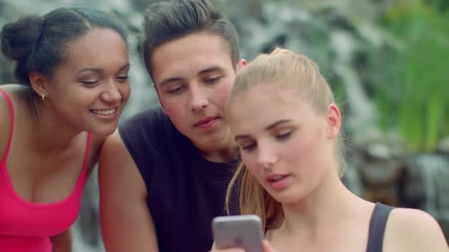 Three Friends Using Smartphone In Park. Young People Talking. Cheerful Friends Smiling. Closeup O...