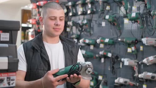A Young Salesman is Holding a Sander in a Hardware Store