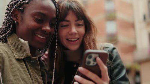 Happy women or two smiling persons using a smartphone standing outdoors, side view