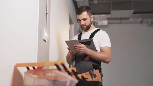 Porträt eines Mannes in einer Firmenuniform mit Werkzeuggürtel und Tablet in der Hand, der einen Zugang konfiguriert