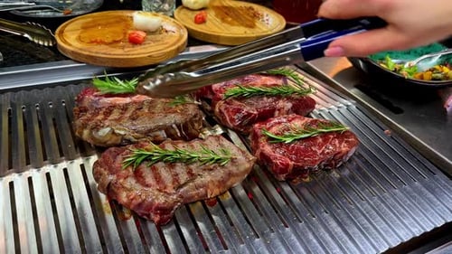 Cook’s holding the barbeque tongs to turn the pieces of meat while cooking on grill.
