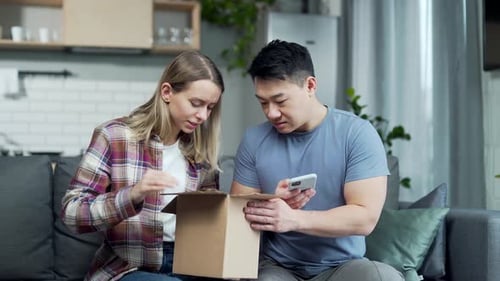 Confused Couple Opens Package on Sofa