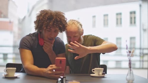 two men sitting in a cafe bar doing a video call with cell phone