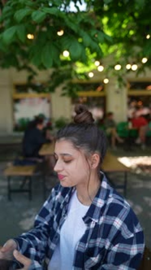 At a Café Terrace a Vibrant Young Lady Has a Phone Call While Leisurely Enjoying a Cocktail