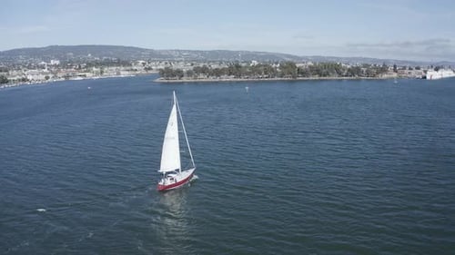 A sailboat slowly slips along as the camera pans up to reveal the bay
