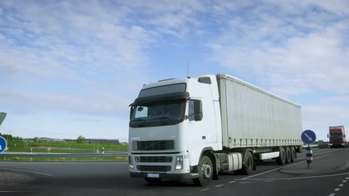 Speeding White Semi Truck with Cargo Trailer Drives on the Highway. Truck is First in the Column of