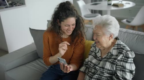 Woman showing smartphone to senior woman on sofa