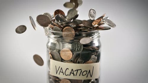 Coins Filling Vacation Savings Jar Close Up