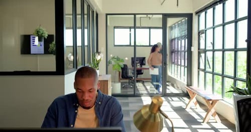 Collègues parlant en se promenant dans le bureau avec une tablette passant un homme afro-américain assis travaillant sur un PC
