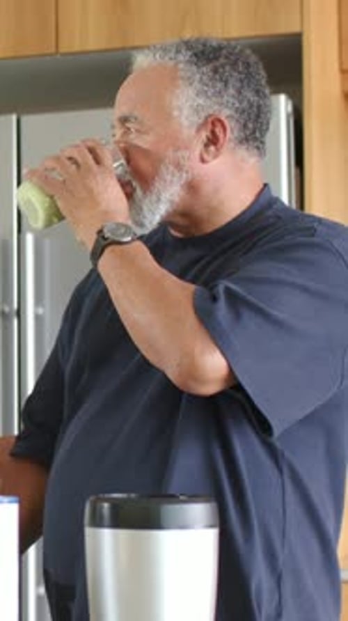 Vertical video: Drinking for thirst, man in kitchen lifting glass with green juice, glancing left
