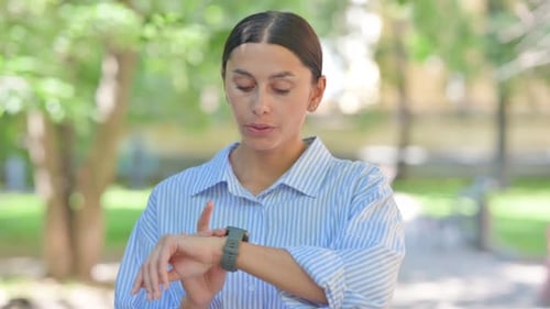 Young Woman Checking Smartwatch in Urban Park