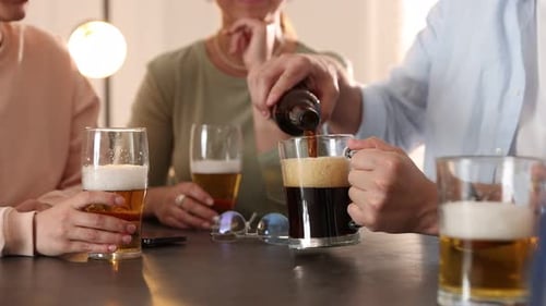 Friends clinking glasses of beer at grey table indoors, closeup. Camera moving up
