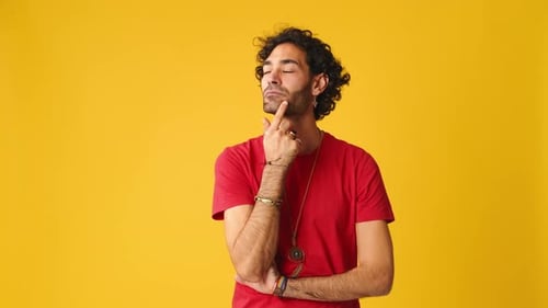 Pensive man rubbing his chin and looking side isolated on yellow background in studio