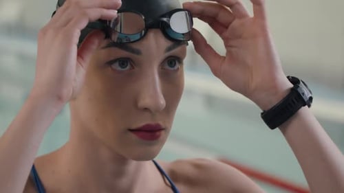 Young Professional Female Swimmer Puts on Glasses for Swimming Training Day in the Pool