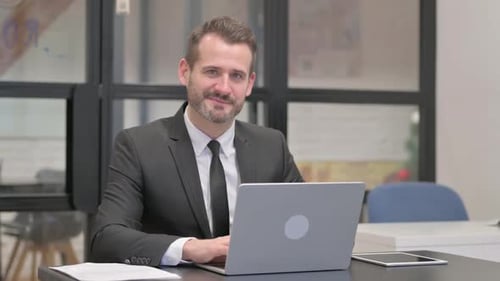 Smiling Businessman Gives Thumbs Up at Laptop